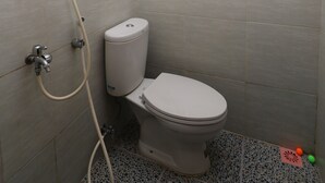Ein kleines Badezimmer mit Fliesen, einer Toilette, einer Duschbrause und einem Toilettenpapierhalter.