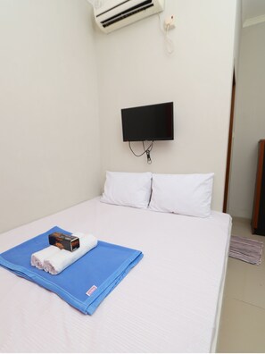 Une chambre d’hôtel avec un lit, un téléviseur à écran plat fixé au mur et une petite boîte posée sur le lit.