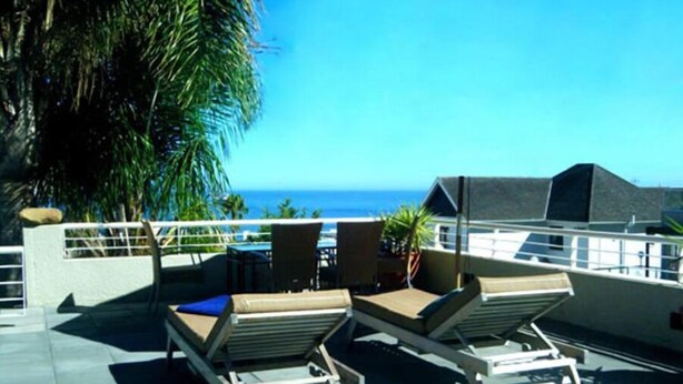 A rooftop terrace with lounge chairs and a table, overlooking a clear blue sky and ocean. - Maison Fontainbleau (Cape Town)