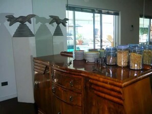A buffet area with a wooden counter, stacked plates, and jars of food. - Maison Fontainbleau (Cape Town)
