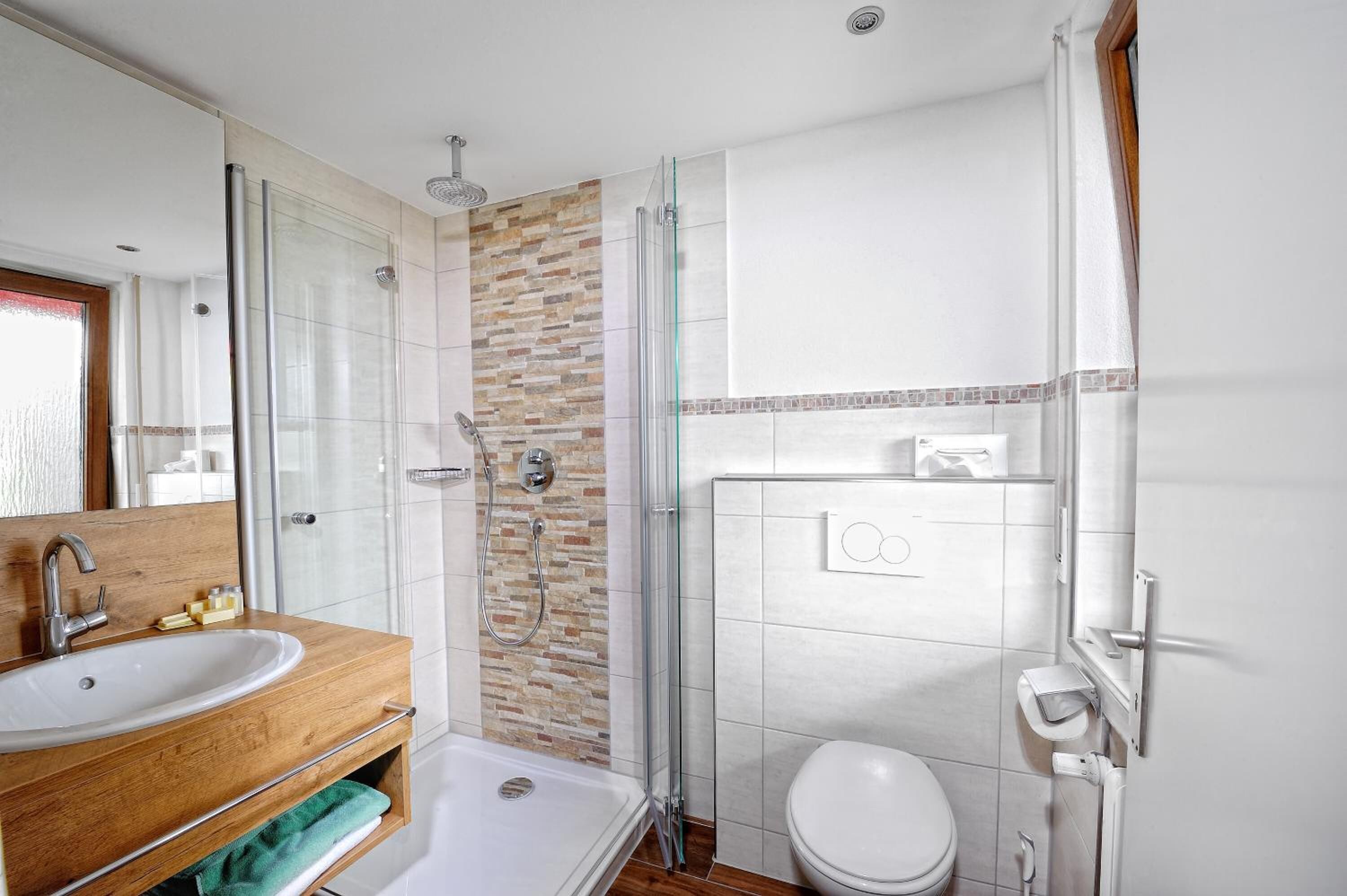 Un baño con tocador de madera, cabina de ducha de vidrio y inodoro blanco.