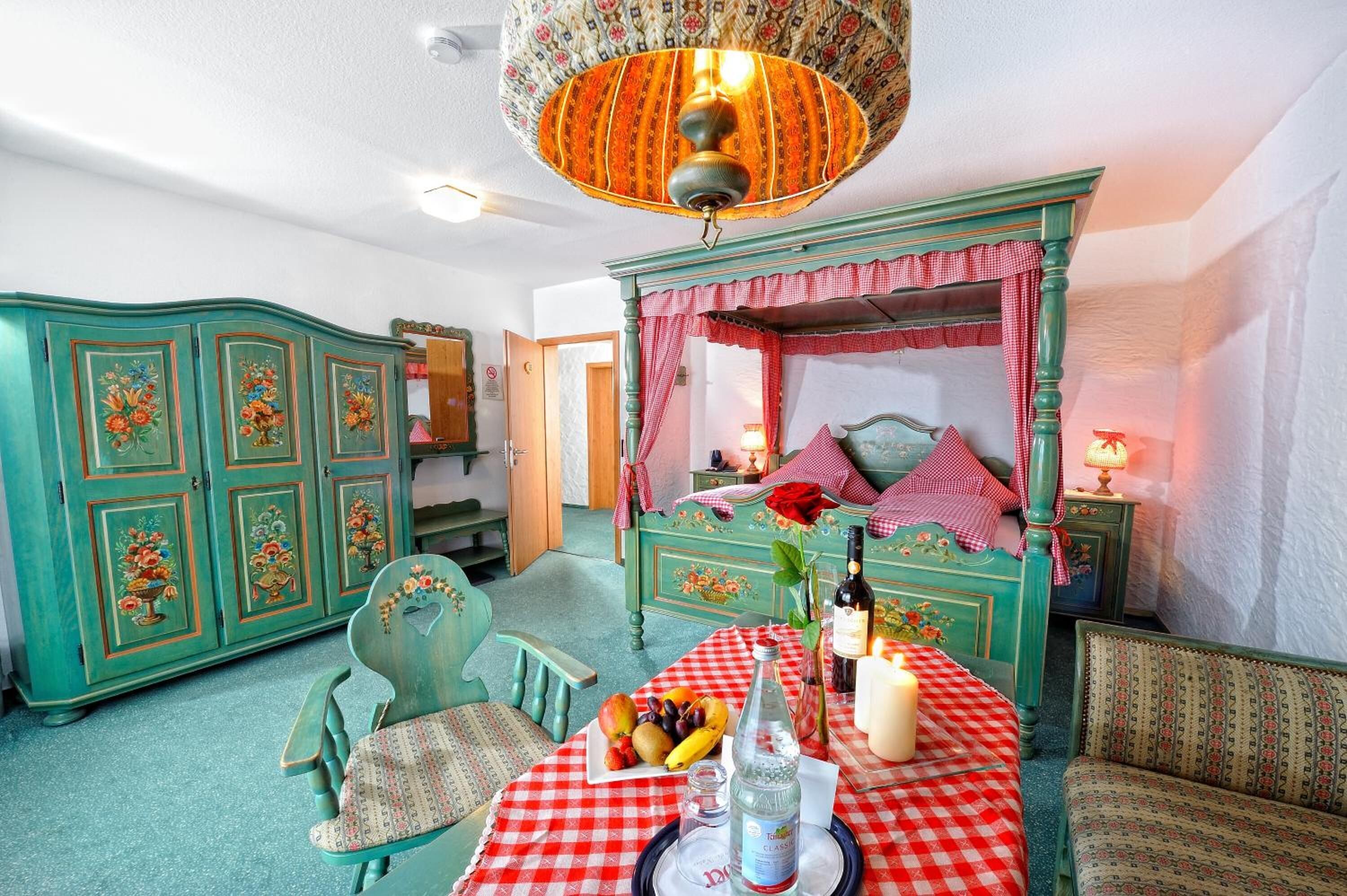 A room with a checkered table set, a bed with a canopy, and a vintage-style chandelier.