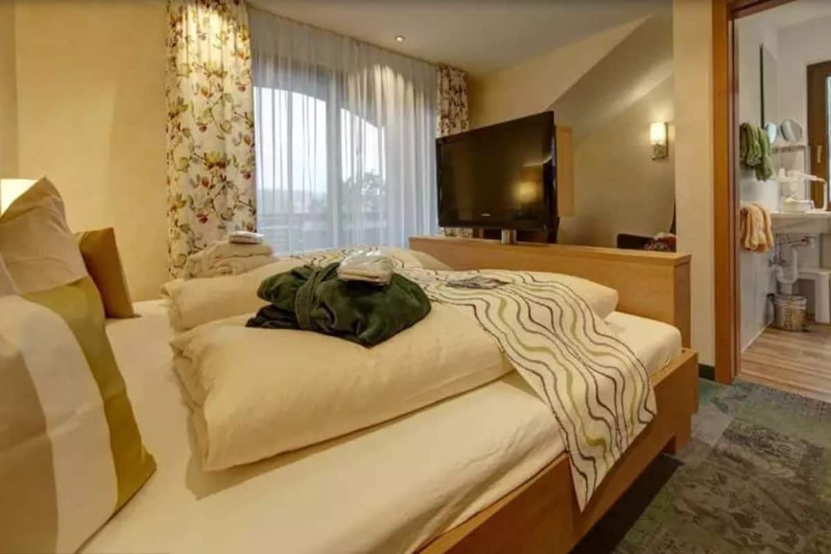 A hotel room with a bed, a TV, a bathroom with a window, and a view of the outside.