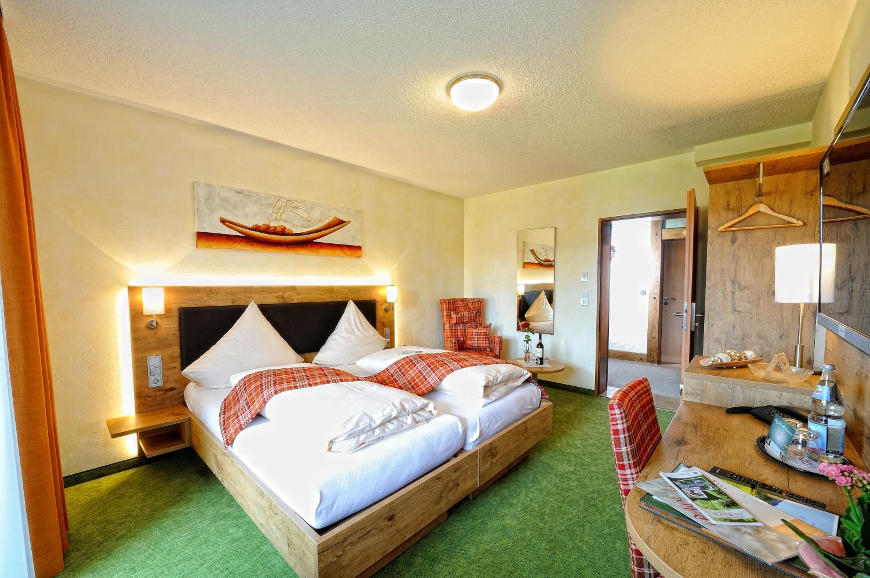 A hotel room with a wooden bed, a desk with a chair, a mirror, and artwork on the walls.