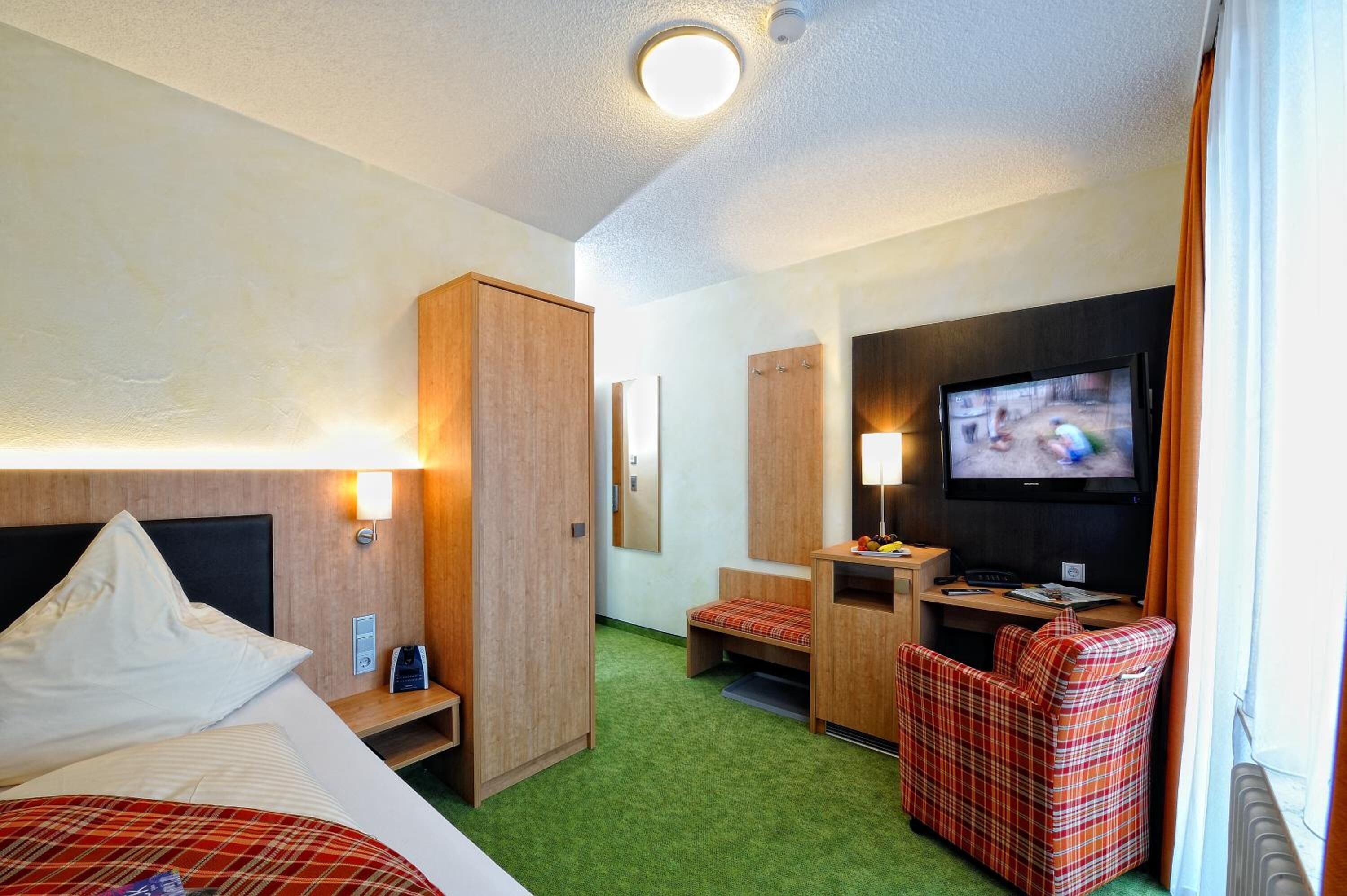 Una habitación de hotel con cama, escritorio, televisor y armario.