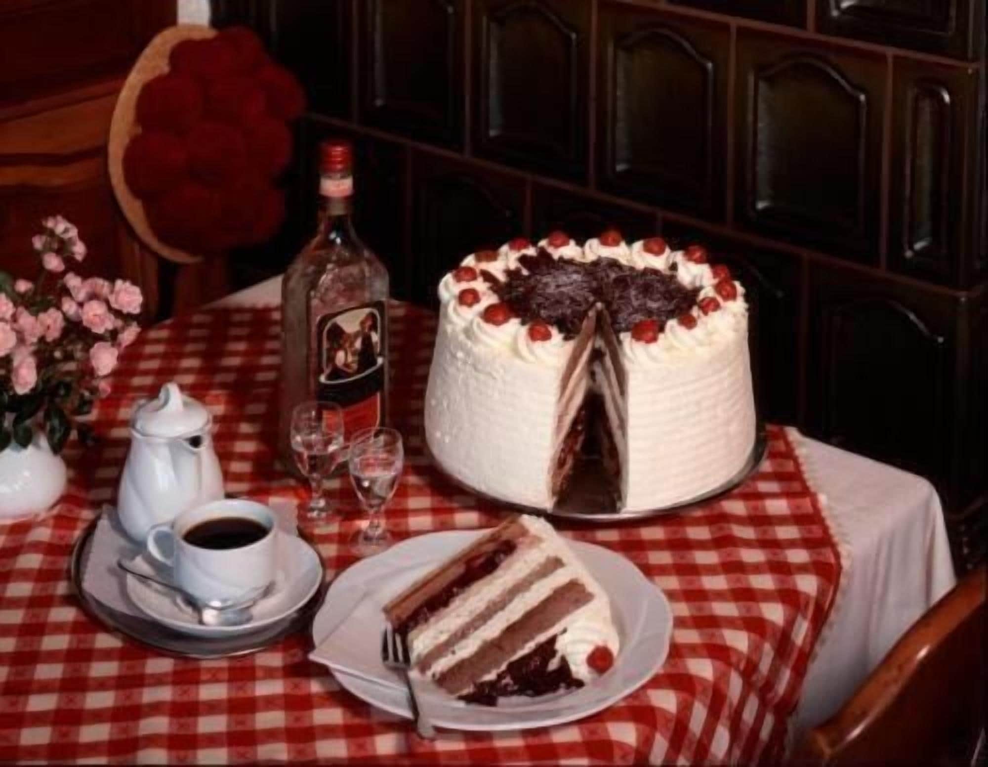 A table with a cake, a bottle, a cup of coffee, and a glass.