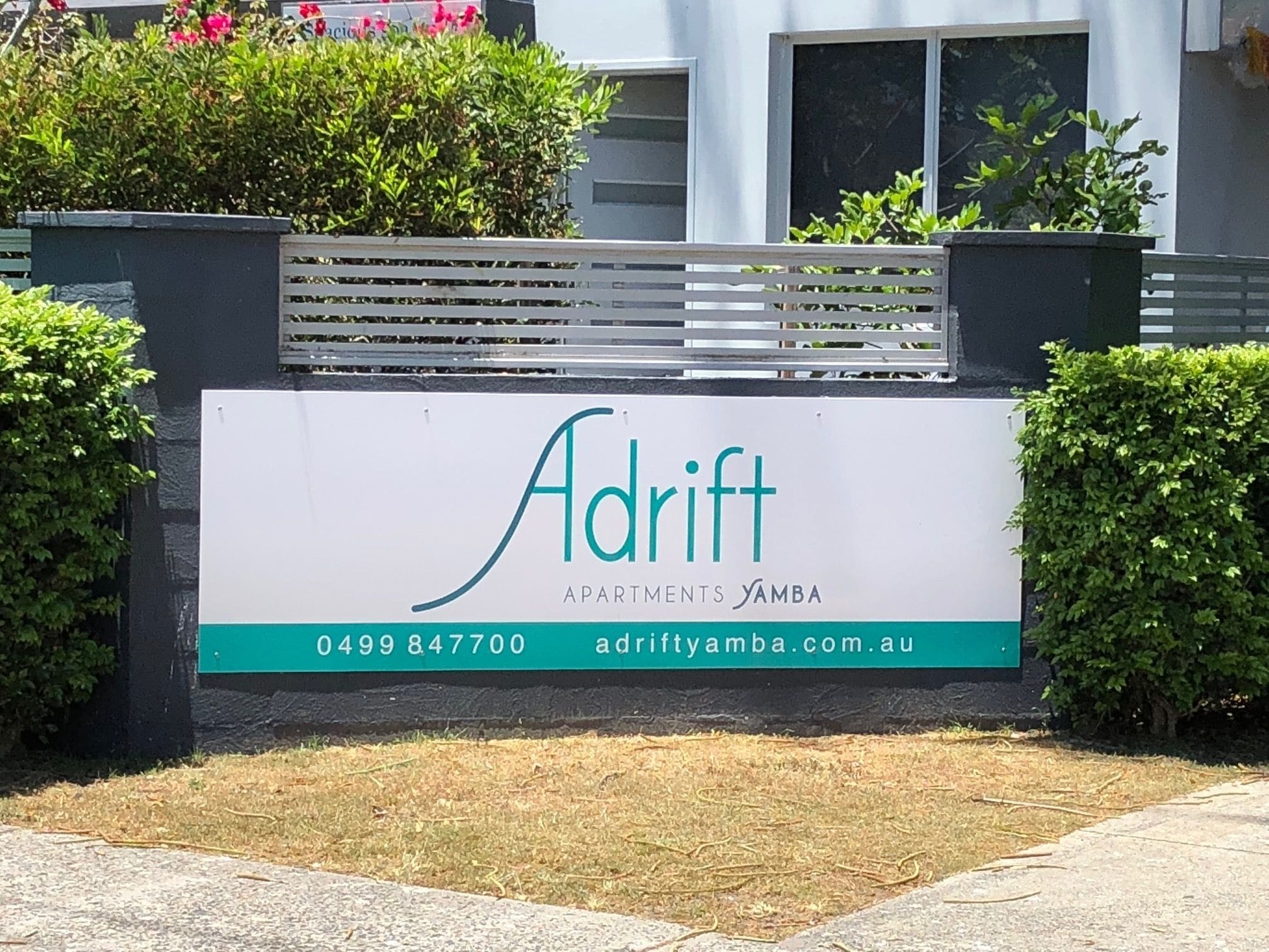 A sign for Adrift Apartments Yamba with contact information.