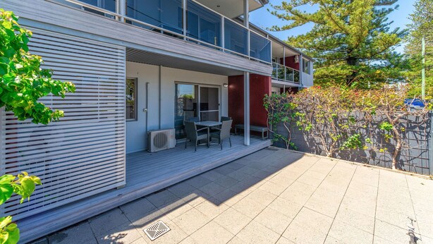 A modern two-story house with a balcony, outdoor seating, and a stone wall. - Adrift Apartments (Yamba)