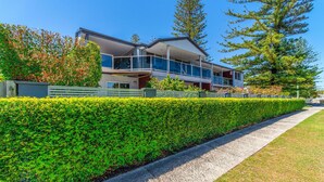 A modern two-story house with a balcony, surrounded by well-maintained hedges and trees. - Adrift Apartments (Yamba)