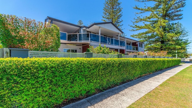 A modern two-story house with a balcony, surrounded by well-maintained hedges and trees. - Adrift Apartments (Yamba)