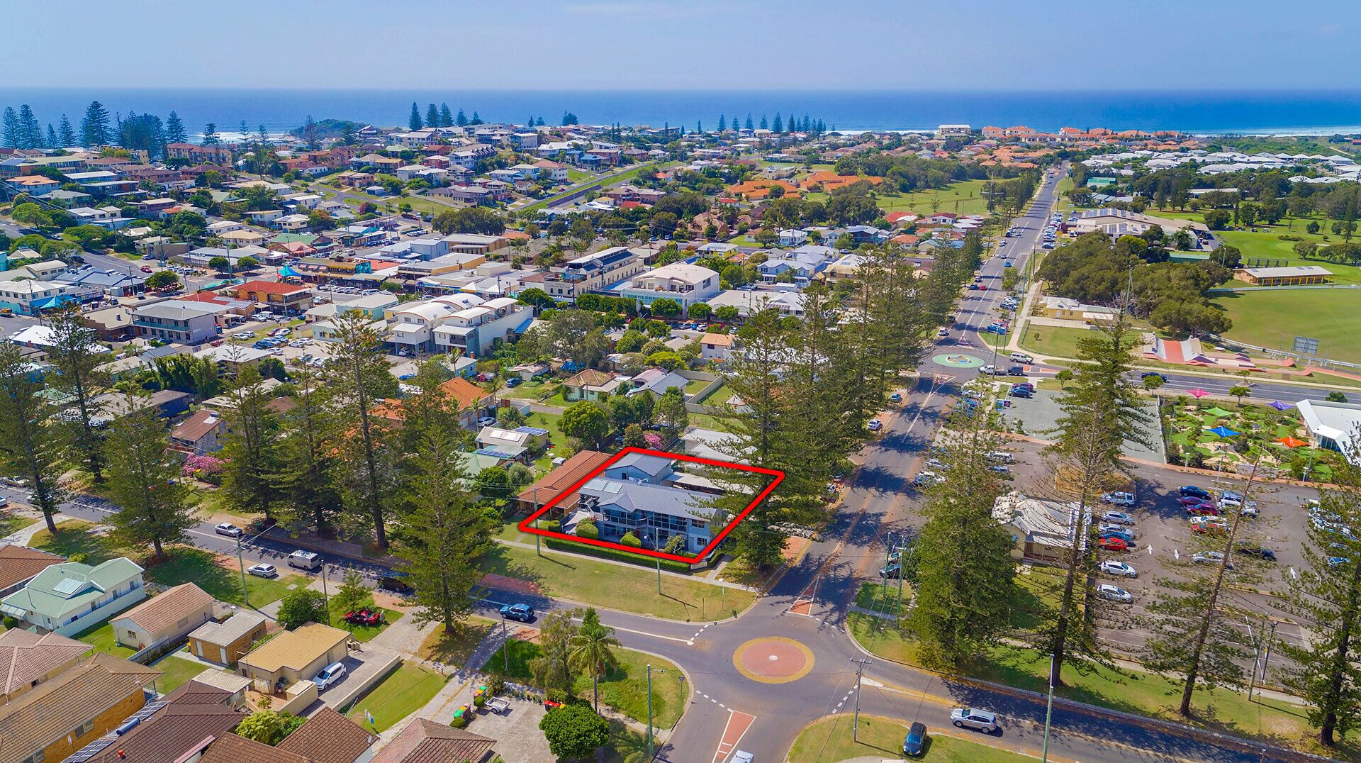 An aerial view of a residential area with a highlighted property featuring a large house with a garage, surrounded by trees and a road.