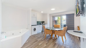 A compact kitchen with a washing machine, a dining area with wicker chairs, and a large window. - Adrift Apartments (Yamba)