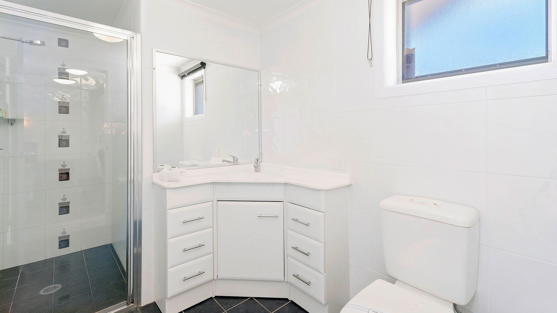 Une salle de bain moderne avec un lavabo d’angle, des toilettes et un espace douche.
