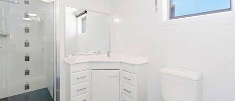 Une salle de bain moderne avec un lavabo d’angle, des toilettes et un espace douche.