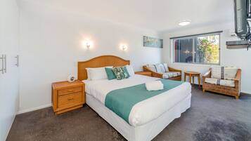 A bedroom with a large bed, two nightstands, a wicker sofa, a small round table, and a window with a view of trees.