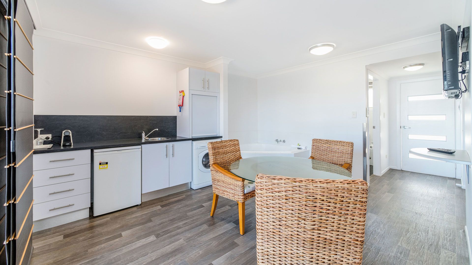 A modern kitchen with white cabinets, a black countertop, and a glass dining table with wicker chairs.