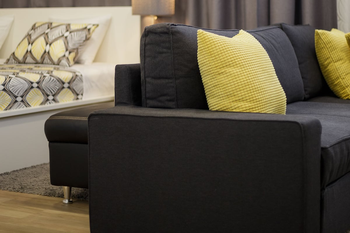Una sala de estar moderna con un sofá oscuro, cojines estampados y una lámpara sobre una mesita.