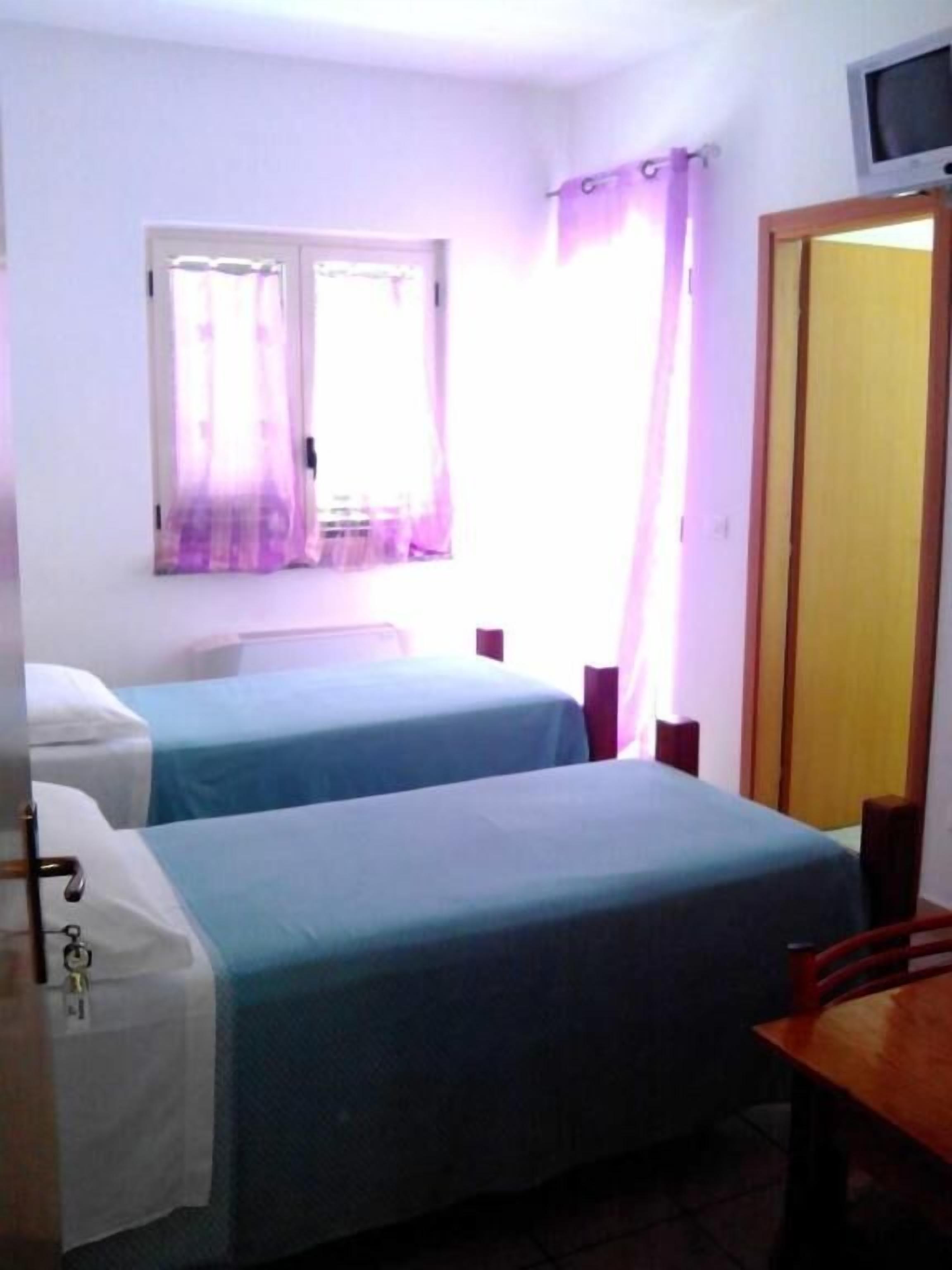 Ein kleines, sauberes Zimmer mit zwei Betten, einem Fernseher und einem Fenster mit Vorhängen.