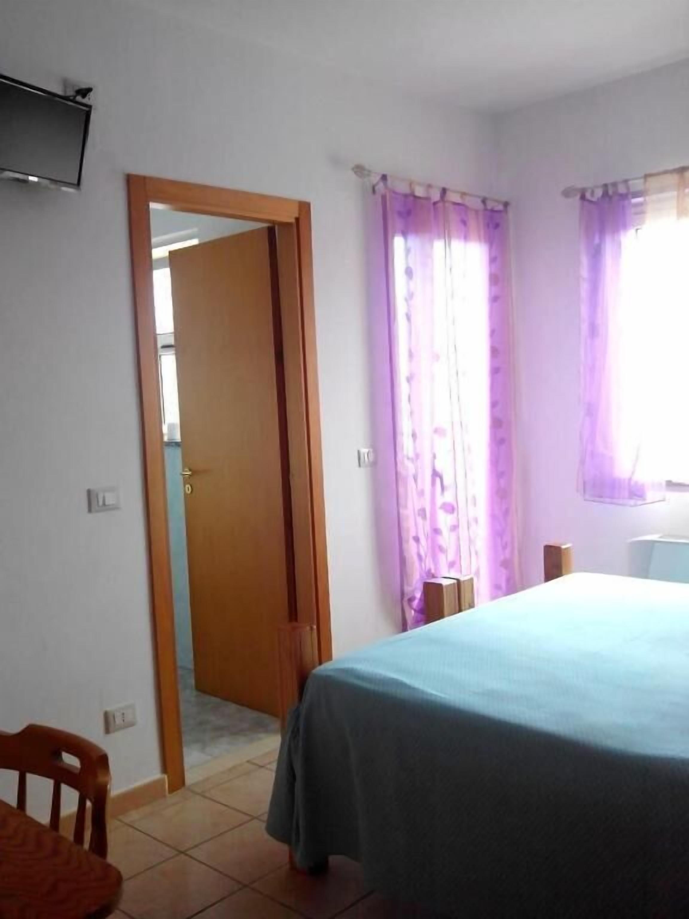 Ein Schlafzimmer mit einem Bett, einer Holztür und einem Fenster mit violetten Vorhängen.