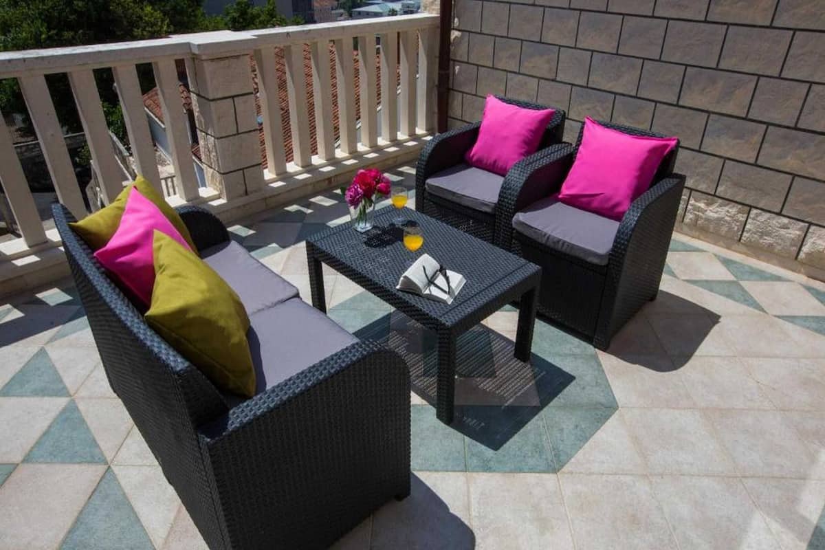 Une terrasse dotée de meubles en osier, notamment deux canapés et une table, agrémentée de coussins roses et verts.