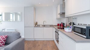 A compact kitchen with white cabinets, a microwave, and a sink. - Roomspace Apartments -Trinity House (Reigate)