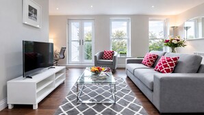 A modern living room with a flat-screen TV, grey sofa, and a patterned rug. - Roomspace Apartments -Trinity House (Reigate)