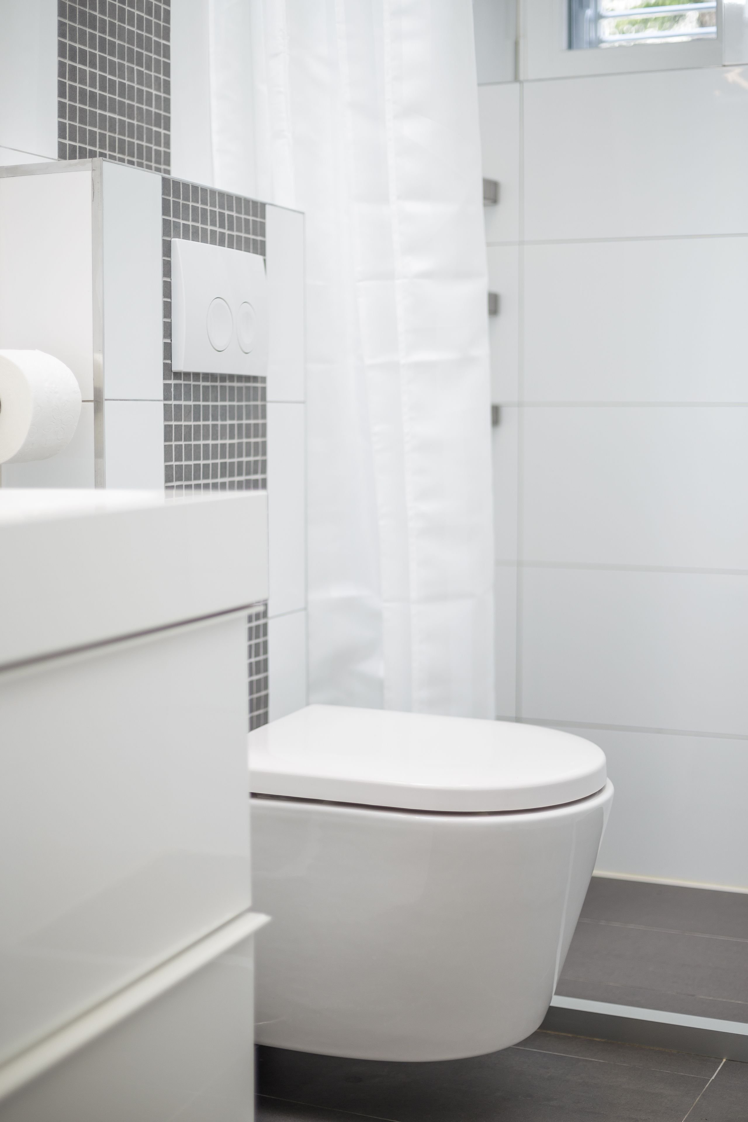 A modern bathroom with a white toilet, a shower curtain, and a tiled wall.