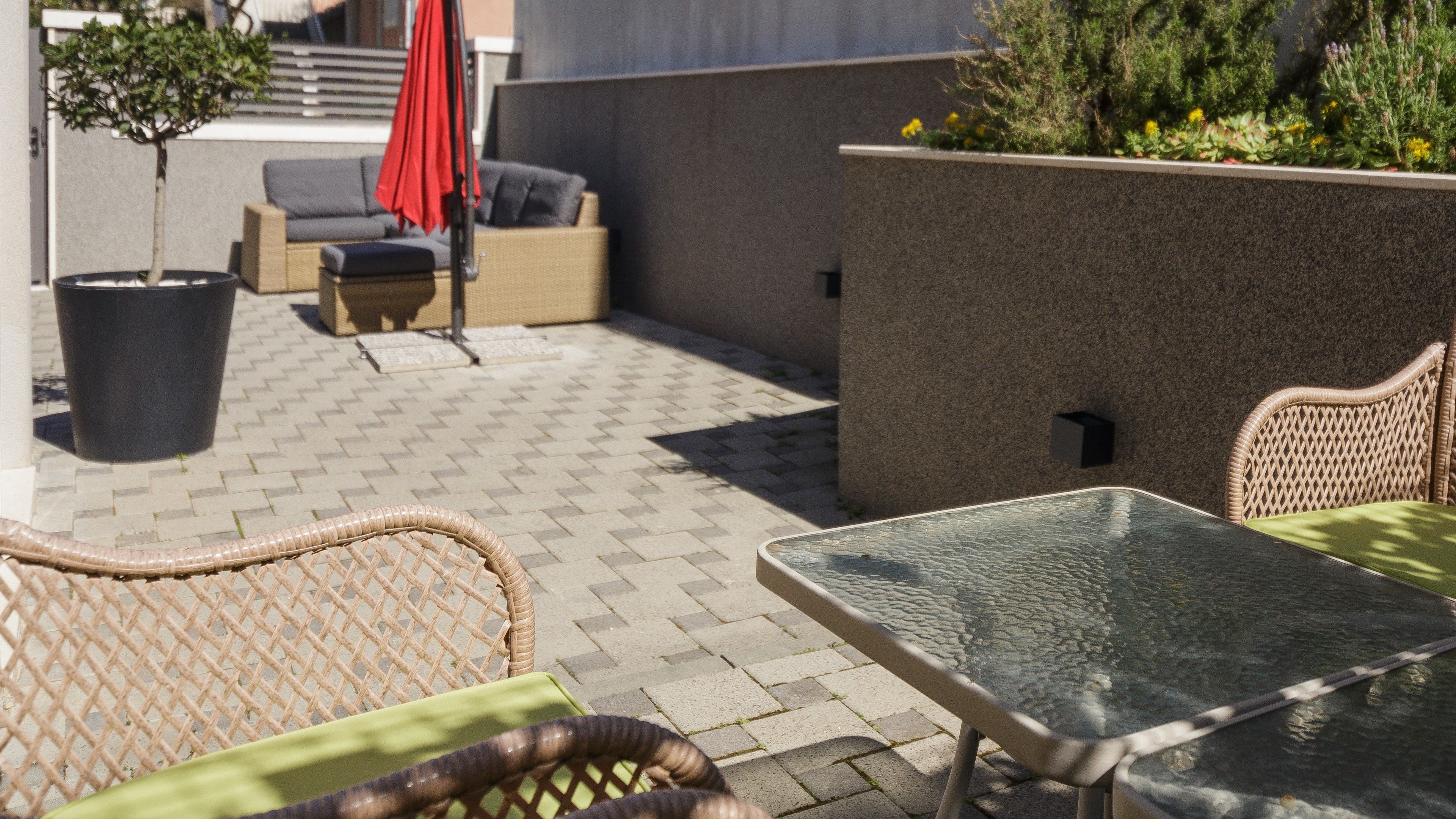 An outdoor patio with wicker furniture, a glass table, and a potted plant.