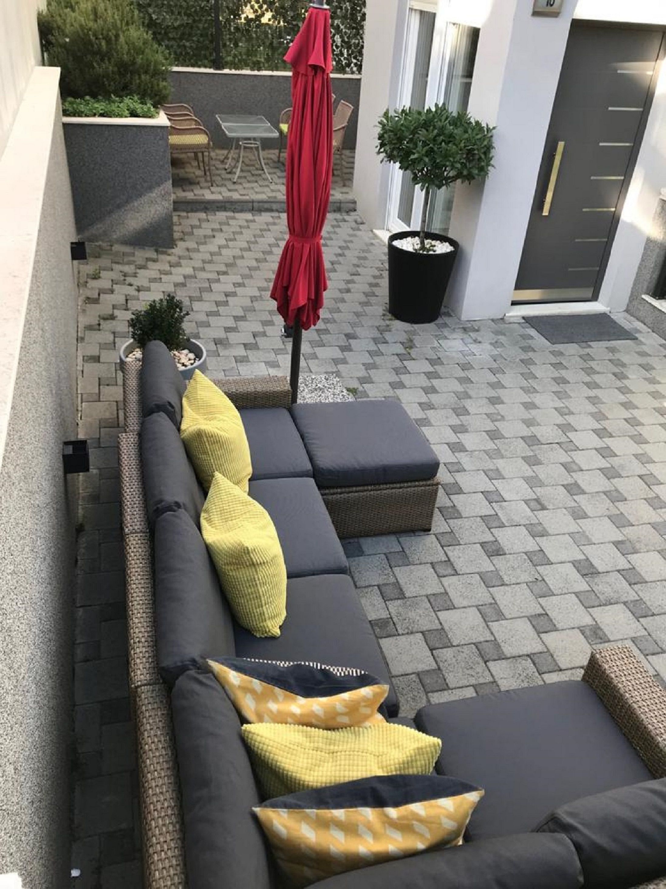 A modern outdoor seating area with a long sofa, cushions, and a red umbrella.