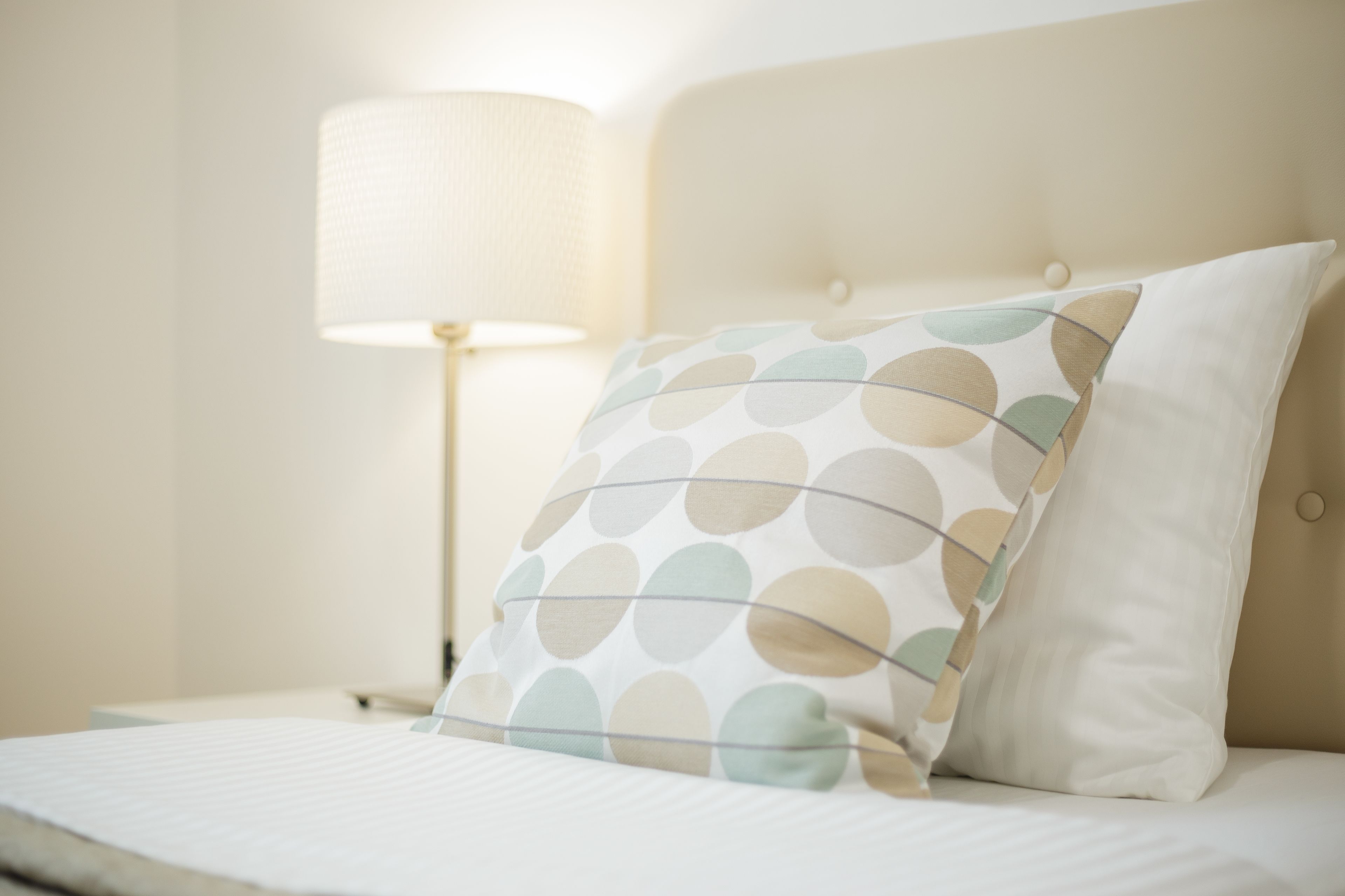 A neatly made bed with a patterned pillow and a bedside lamp.