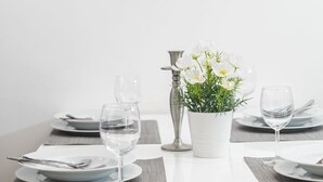 A dining table set with plates, cutlery, and a vase of flowers, with a cityscape painting in the background. - Holiday Home Aspalathos (Split)