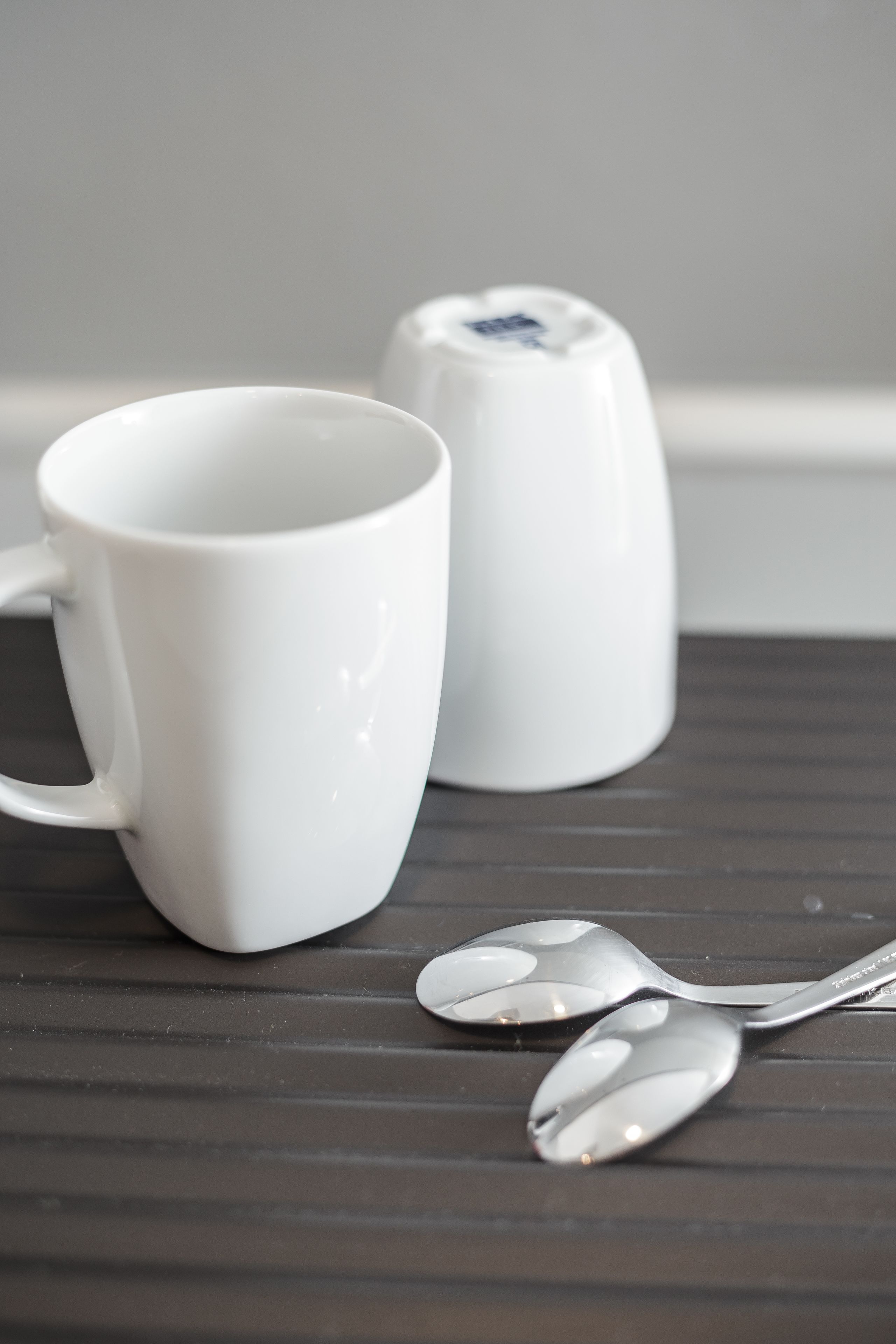 Deux tasses en céramique blanche et deux cuillères sur une surface en bois foncé.