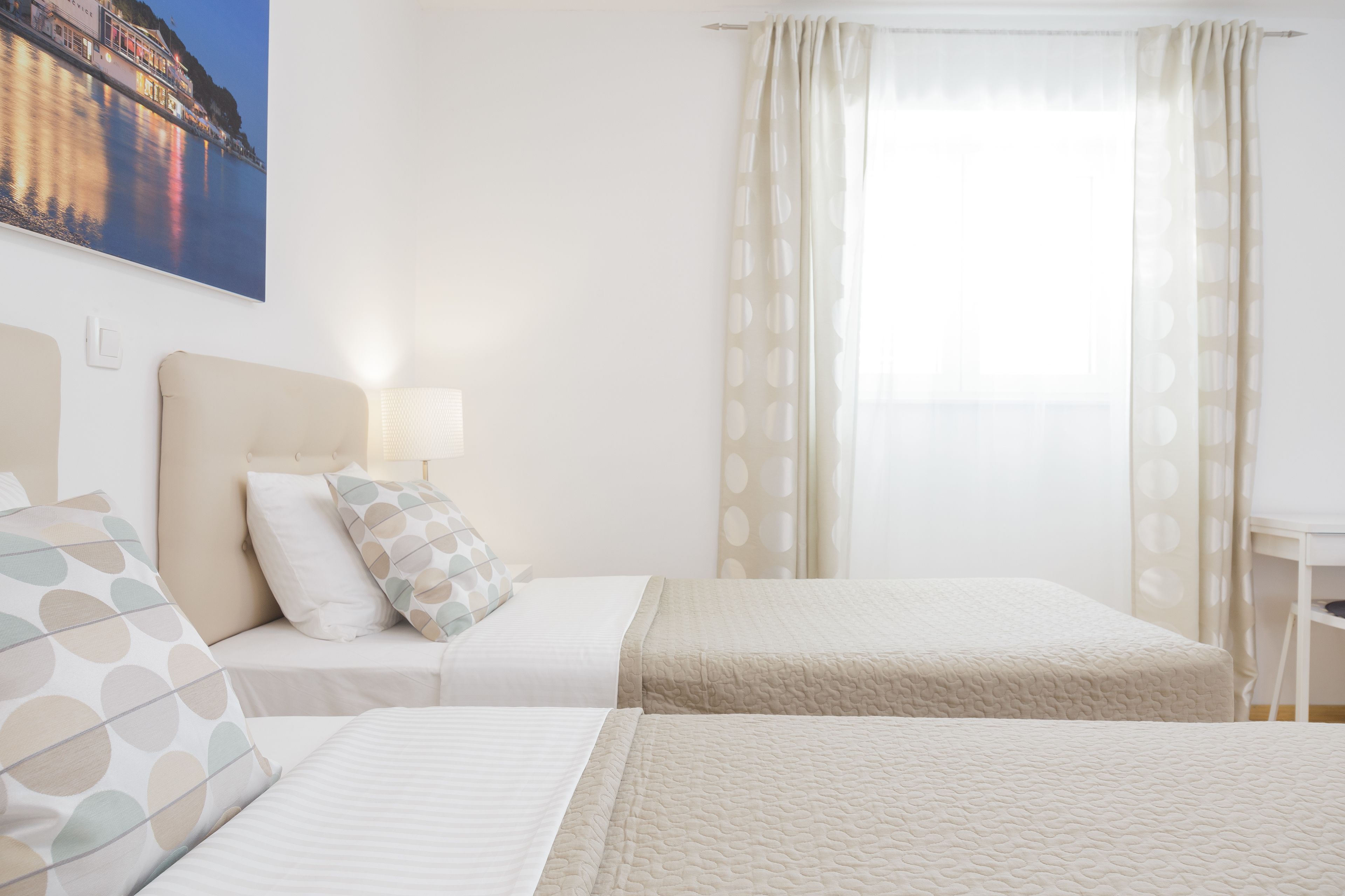 Une chambre d’hôtel avec deux lits, une table de chevet, une lampe et un tableau représentant un paysage côtier.