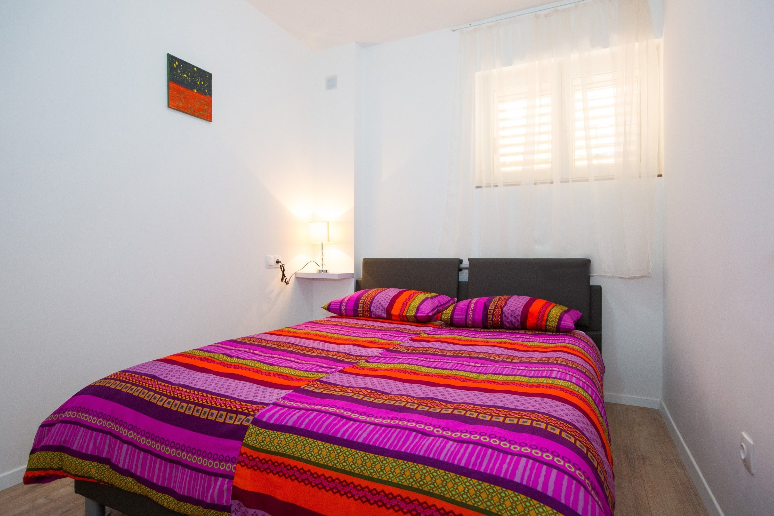Un dormitorio con cama, mesita de noche, lámpara y ventana con cortinas.