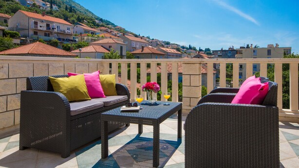 Une terrasse meublée de mobilier en osier, avec une table et une vue sur une ville située sur une colline.