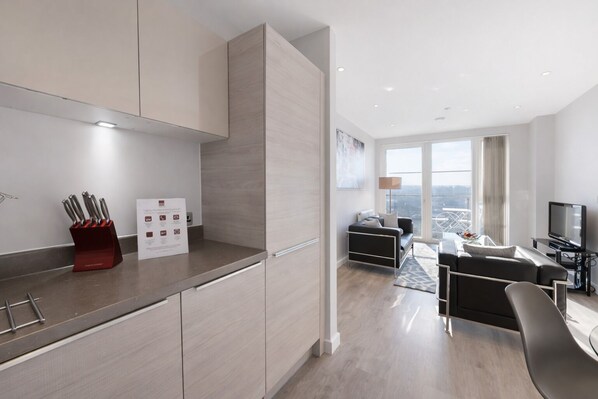 A modern kitchen with a built-in oven, a dining area with a glass table, and a living room with a sofa and a TV. - Roomspace Apartments -Vertex House (Croydon)