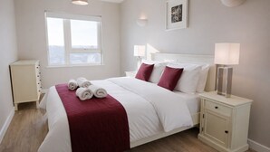 Une chambre à coucher avec un lit, des tables de chevet, une fenêtre et un tableau accroché au mur.