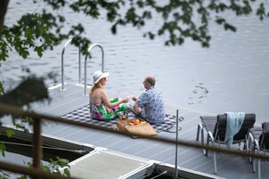 Um casal sentado em um píer, com um barco ao fundo.