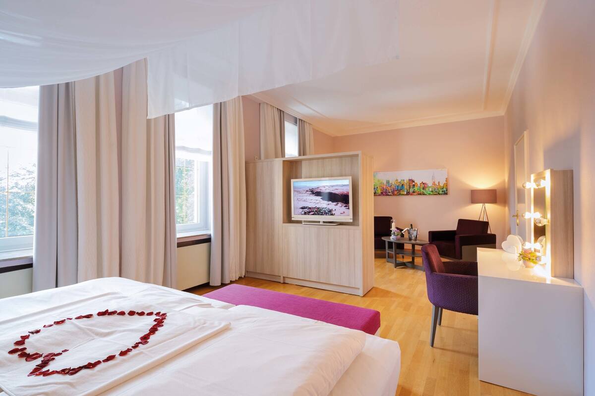 A hotel room with a bed, a TV, a desk with a chair, and a window with curtains.