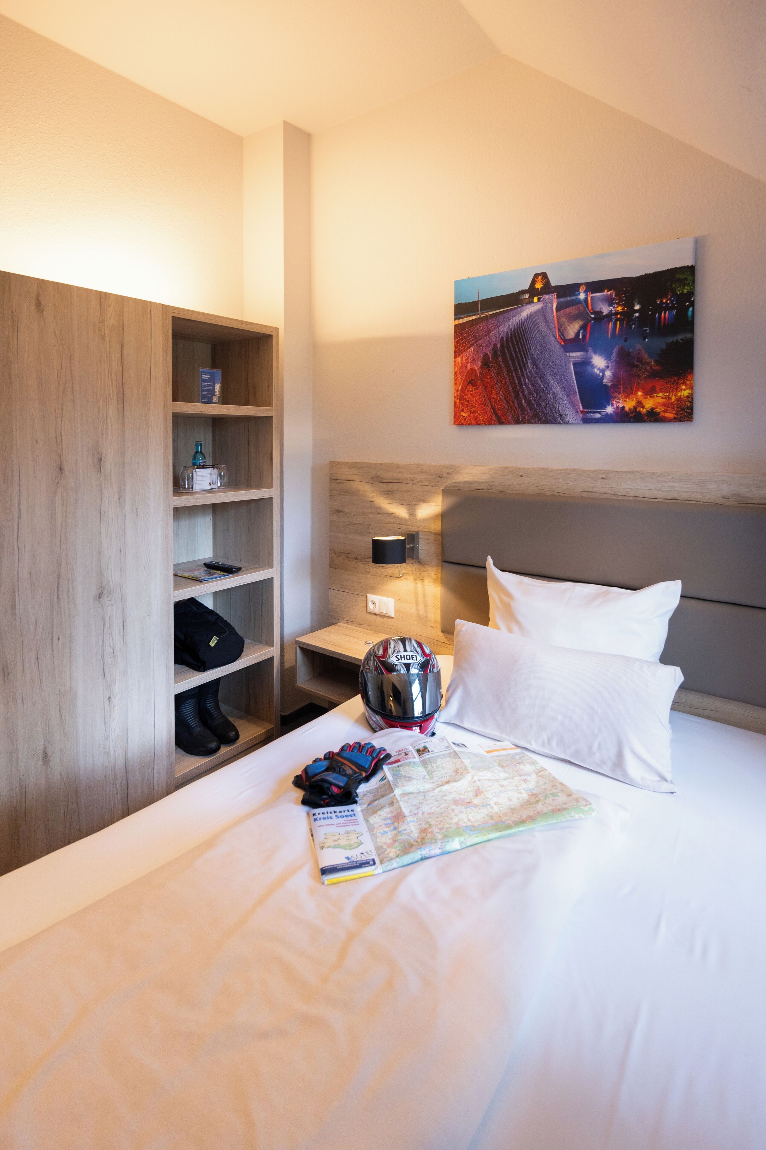 Ein Hotelzimmer mit einem Bett, einem Holzschrank, einem Nachttisch, einem Helm und einem Bild an der Wand.
