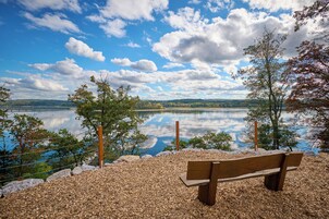 Um banco com vista para um lago tranquilo, céu claro e colinas ao longe.
