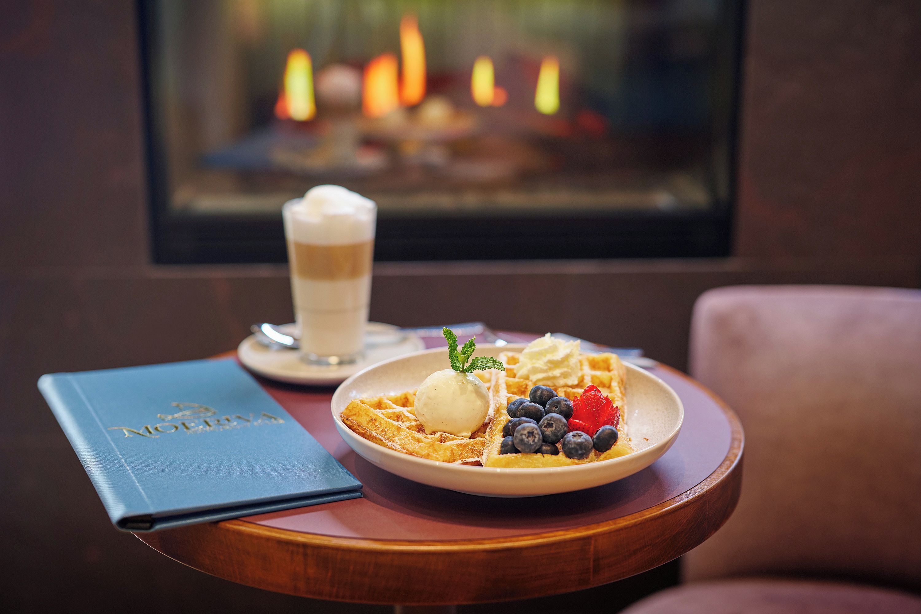 A dessert plate with ice cream, blueberries, and a strawberry on a wooden table.