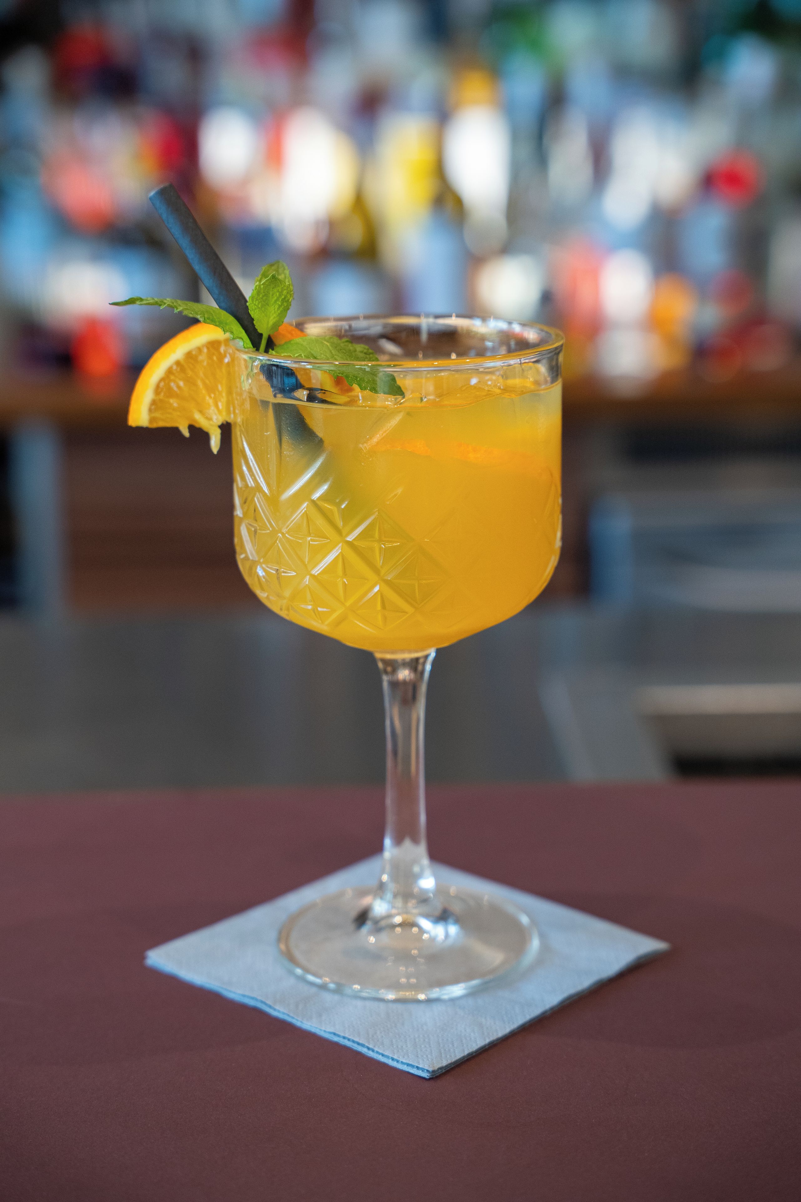 A cocktail glass with a lime wedge and mint leaves on a bar mat.