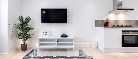 A modern kitchen with a built-in oven, a stainless steel range hood, and a flat-screen TV mounted on the wall.