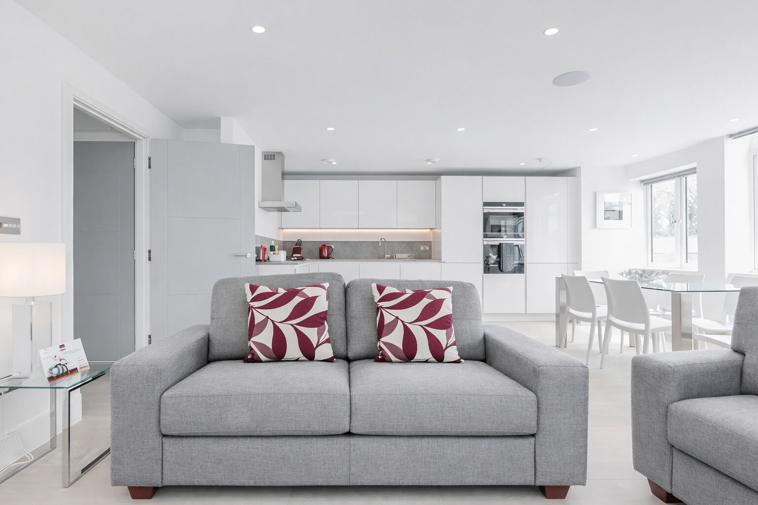 A modern living room with a grey sofa, two patterned throw pillows, and a glass coffee table.