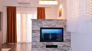 A modern living room with a stone wall, a flat-screen TV mounted on it, and a large window with curtains. - City Apartments Lani 4 (Dubrovnik)