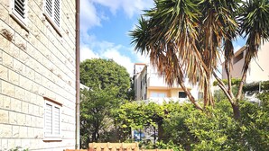 A children's playhouse with a red roof and a green door, situated on a tiled patio with a white fence and a potted plant nearby. - City Apartments Lani 4 (Dubrovnik)