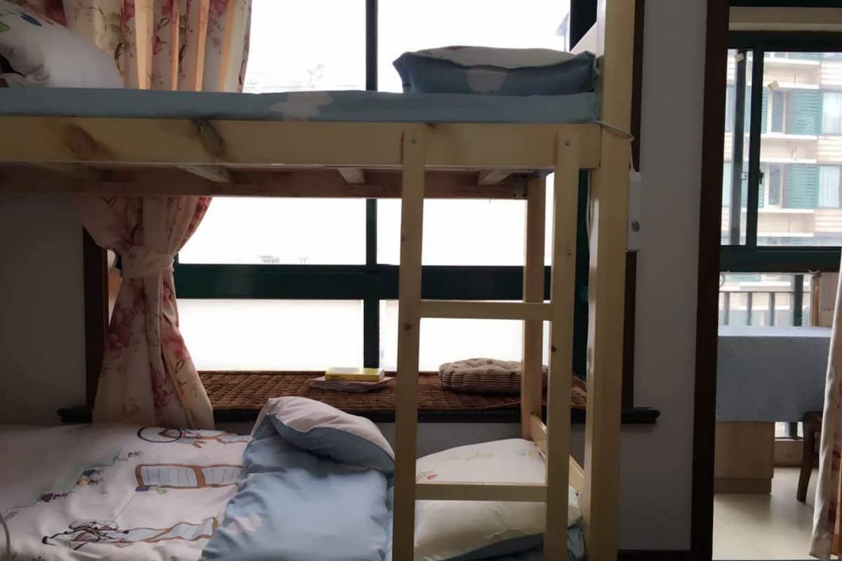 A bunk bed with a wooden frame, a window with curtains, and a view of buildings outside.