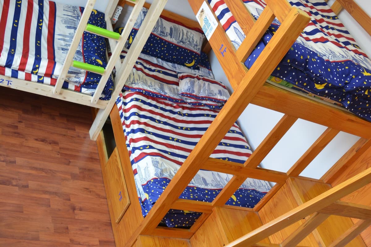 A bunk bed with a wooden ladder, two beds with striped bedding, and a wooden floor.