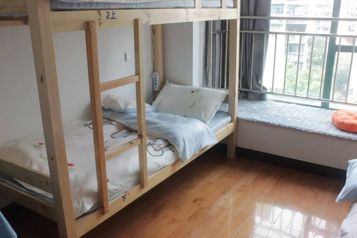 A bunk bed room with a window, wooden flooring, and a small window seat.